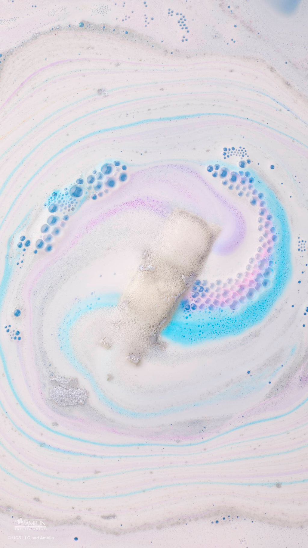 A silver, "OUTATIME" DeLorean car-shaped bath bomb completely dissolves into thick, creamy white foam. Swirls of bright blue and soft purple bubbles radiate outwards, creating a colourful, marbled pattern across the surface of the bathwater.
