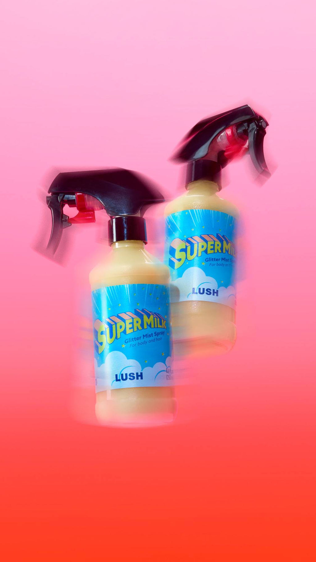Two bottles of Lush 'Super Milk' Glitter Mist Spray appear to float with a dynamic motion-blur effect against a vibrant pink-to-red gradient background. The cream-coloured liquid and bright blue labels stand out in the energetic composition.